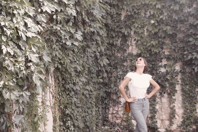 Woman with hands on hip standing against plants