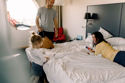 Man talking to happy woman looking at daughter standing by bed
