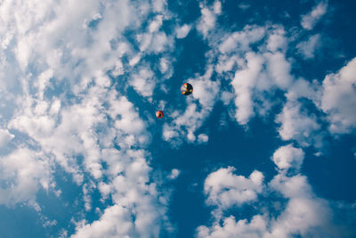 Low angle view of hot air balloons flying against cloudy blue sky