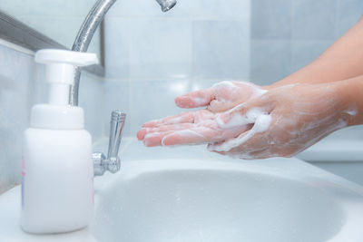 Cropped image of woman washing hands at faucet