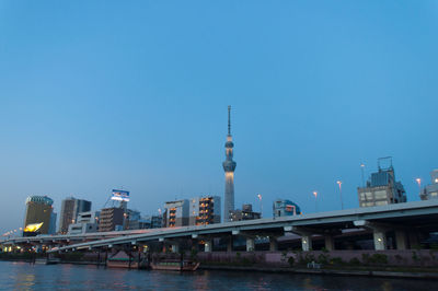 Illuminated tokyo sky tree in city by river against clear sky at dusk