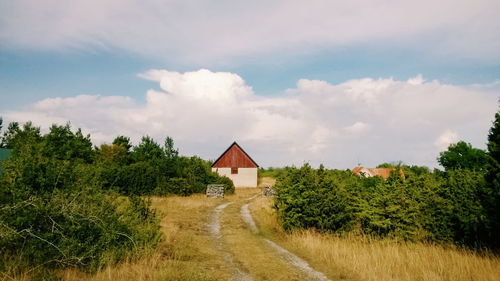 House amidst trees on grassy field against cloudy sky