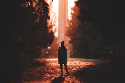 Rear view of woman standing on footpath in city during sunset