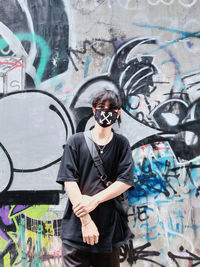 Full length of man wearing sunglasses standing against graffiti wall