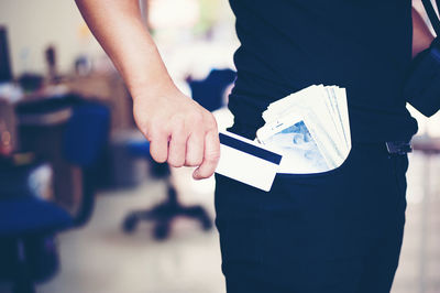 Midsection of businessman with paper currency in pocket holding credit card