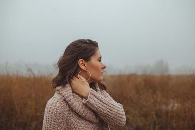 Young woman looking away while standing on field against sky during winter