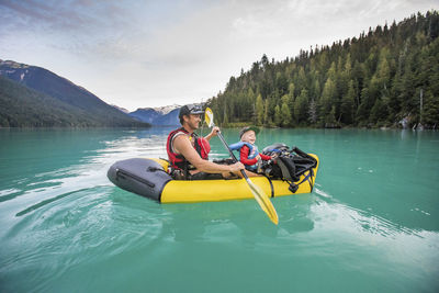 Father and son laughing, enjoying paddling trip on turquoise lake.
