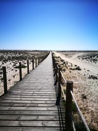 Boardwalk leading to wooden structure against clear blue sky