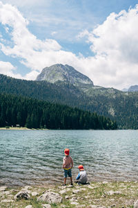 People on lake by mountains against sky