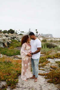 Mixed race couple posing for maternity shoot on beach