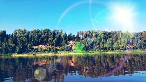 Reflection of trees in water against blue sky