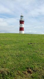 Lighthouse on field against sky