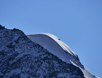 Low angle view of snowcapped mountains against clear blue sky