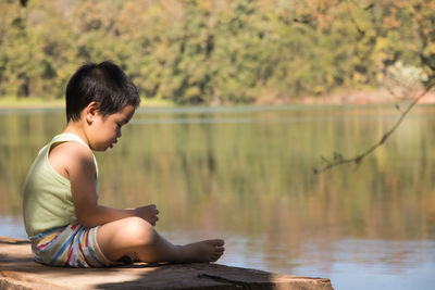 Side view of boy sitting by lake