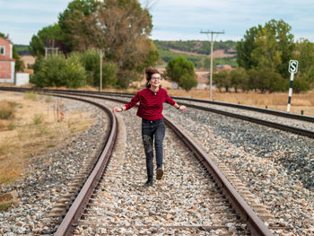 Full length of smiling teenage girl walking on railroad track