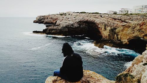 Rear view of woman sitting on rock by sea