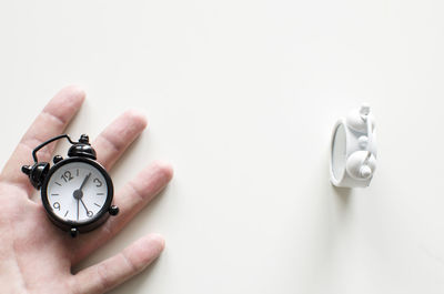 Close-up of hand holding clock over white background