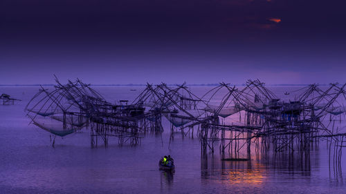 Fishing net in sea against sky at sunset