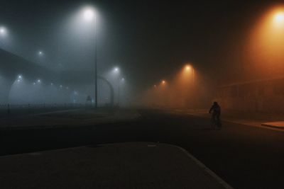 Rear view of man walking on illuminated street at night