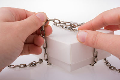 Close-up of hand holding tying chain on box over white background