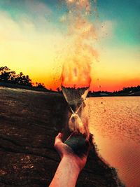 Close-up of hand holding leaf against sky during sunset