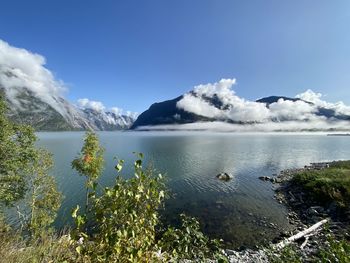 Scenic view of fjord against mountain covered in clouds with clear sky above