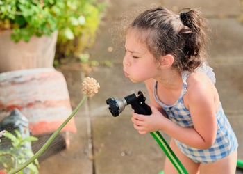 Young girl is watering plants in the backyard while wearing a bathing suit