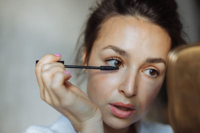 Brunette woman paints eyelashes with black mascara