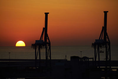 Silhouette cranes against orange sky during sunset