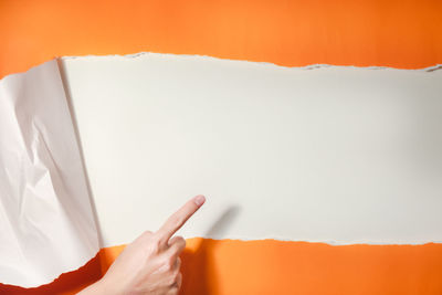 Close-up of hand holding paper against white wall