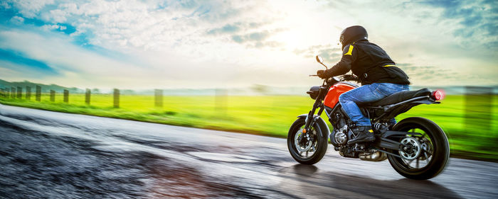 Man riding motorcycle on road against cloudy sky