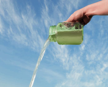 Cropped image of person hand holding drink against cloudy sky
