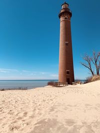 Lighthouse on beach against clear blue sky