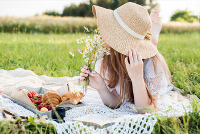 Midsection of woman holding hat on field