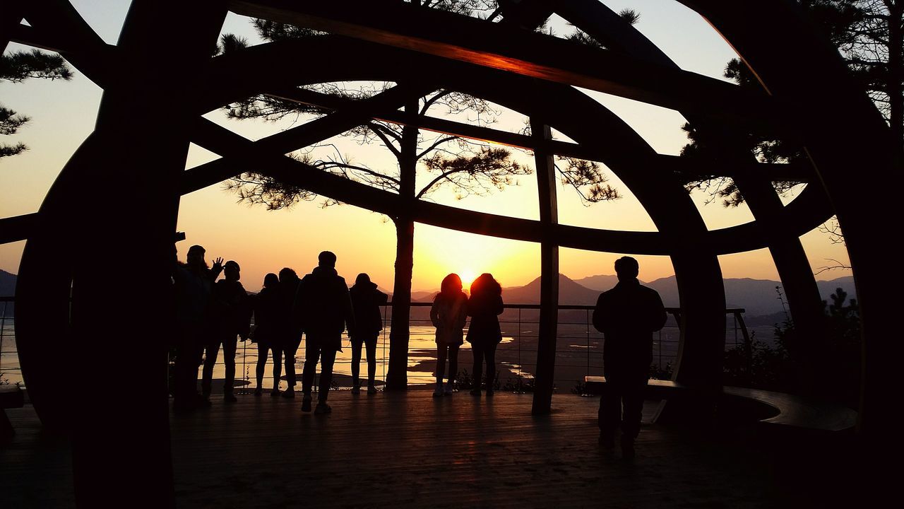 sunset, silhouette, orange color, men, lifestyles, leisure activity, standing, sun, sky, water, built structure, person, architecture, reflection, sunlight, tourist, outdoors, nature