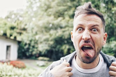 Portrait of man sticking out tongue against trees