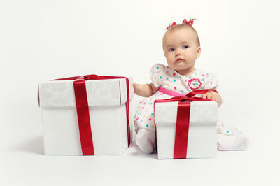 Cute baby girl with christmas gifts sitting against white background