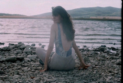 Woman sitting on rock at beach against sky