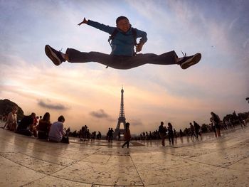 Fish-eye view of man jumping against eiffel tower during sunset