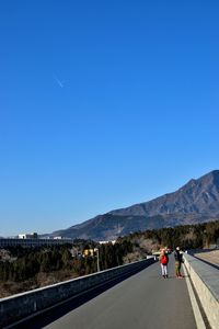 Road leading towards mountains against clear blue sky