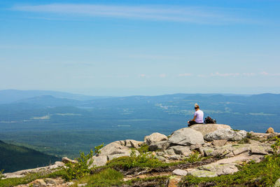 Woman sitting on rock by sea against sky