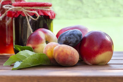 Fresh fruits and homemade jars of jam on wooden table in blurred natural garden background. 