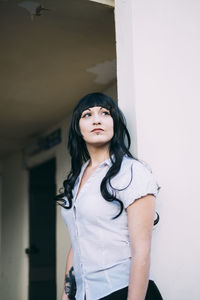 Woman looking away while standing against wall