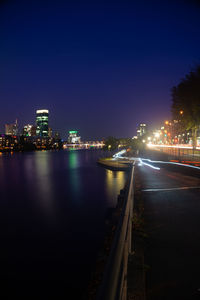 Illuminated city by river against sky at night