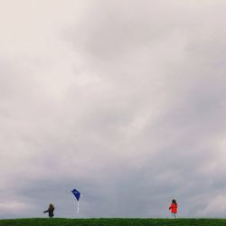 People on grassy field against cloudy sky