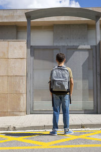 Rear view of boy with backpack standing against metal door during sunny day