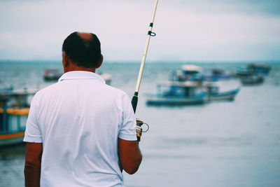 Rear view of man holding sailboat in sea