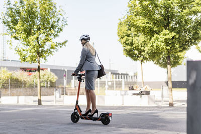 Businesswoman wearing high heels riding electric scooter on the street