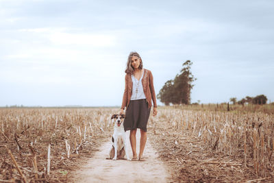 Full length portrait of young woman standing on field against sky