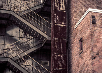 Low angle view of weathered air duct by fire escape on building